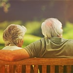 Senior couple sitting on a bench talking about a not-for-profit retirement community. 